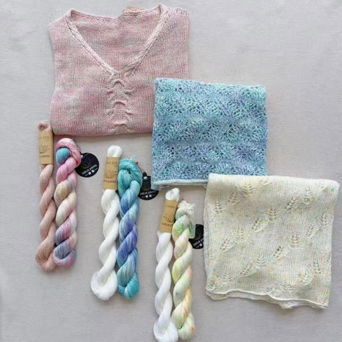 Knitted vest and two lace shawls laid flat with Lotus Yarns Linen 100 skeins